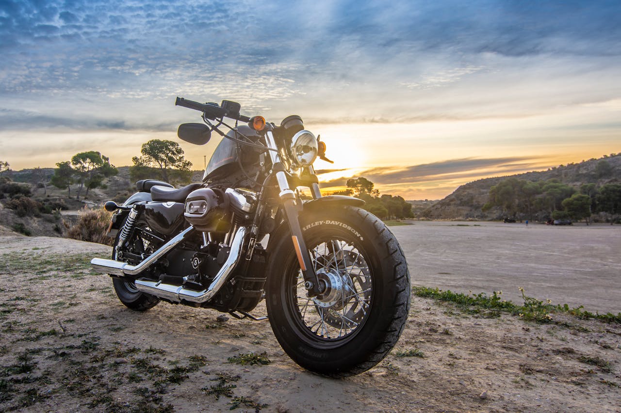 services-02 A Harley Davidson motorcycle parked outdoors against a stunning sunset sky, perfect for adventure and travel imagery.